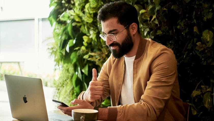 man in brown jacket sitting at a table looking at laptop
