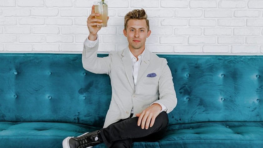man in gray blazer raising drinking glass while sitting on sofa