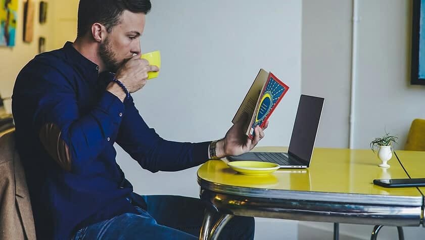 person reading book while drinking beverage