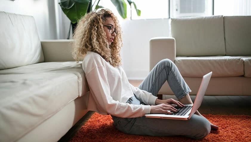 woman sitting on floor and leaning on couch using laptop