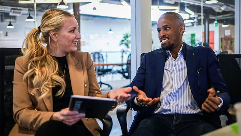 man in black suit jacket sitting beside woman in brown blazer