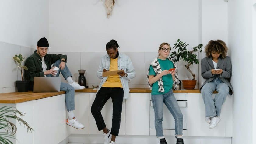 Casual and diverse colleagues using gadgets in a modern office kitchen area.